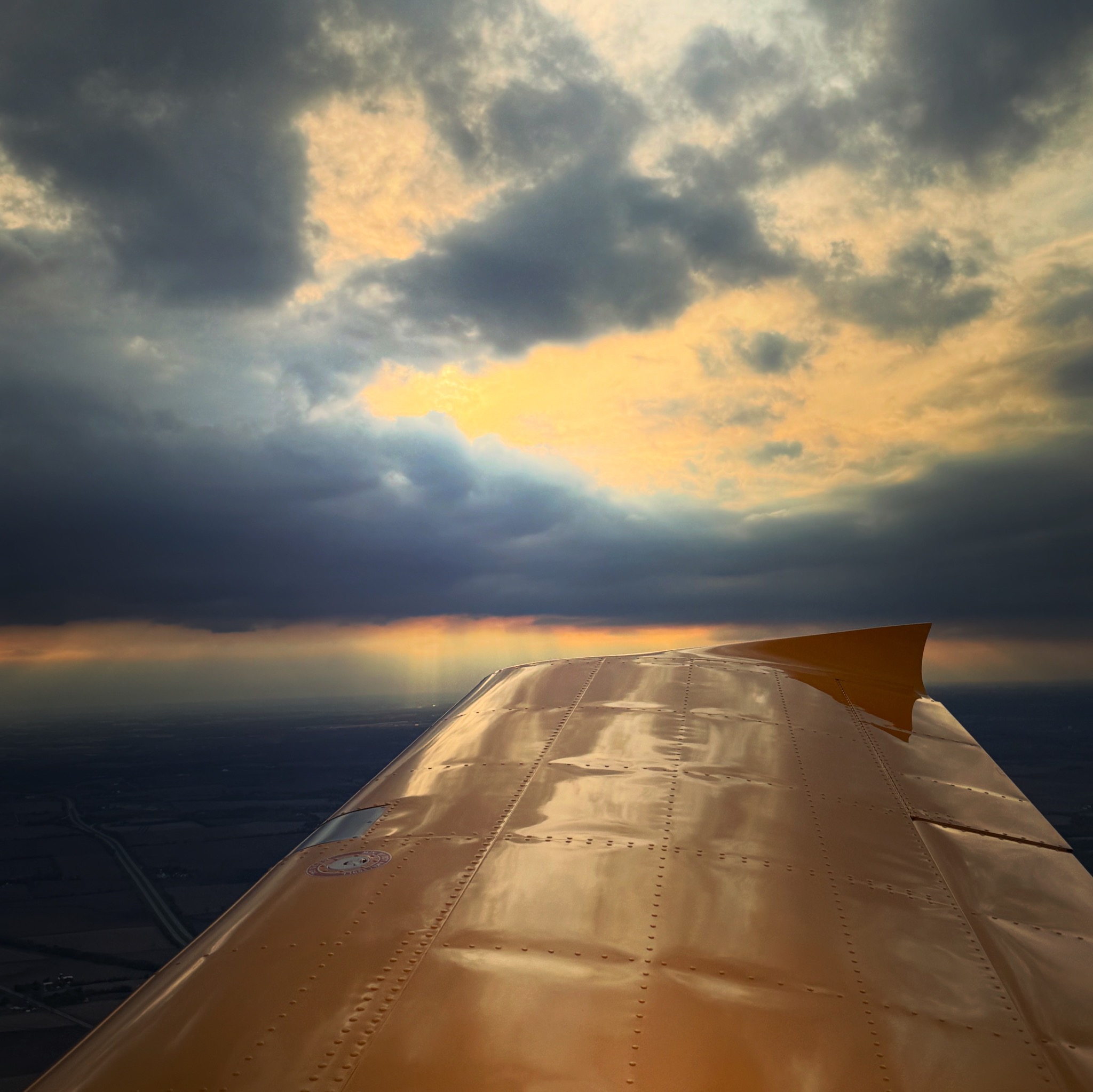 Aircraft wing beneath dramatic clouds at sunset